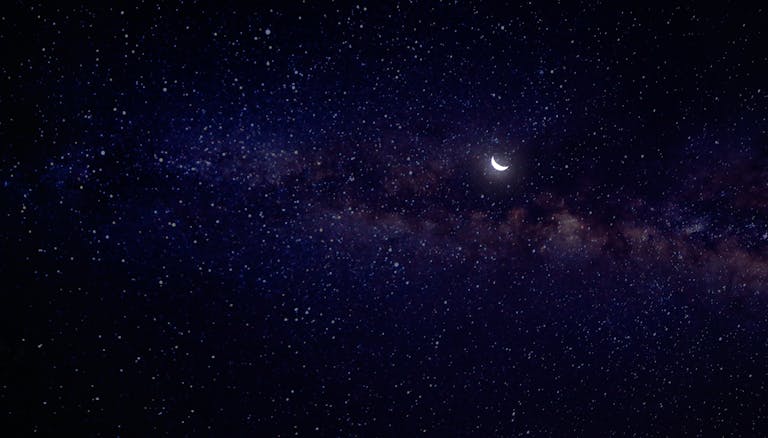 A breathtaking view of the starry night sky featuring the Milky Way and a waning crescent moon.